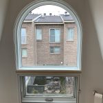 Arched Bquiet Soundproof window in a room, providing a view of a residential backyard and neighboring buildings.